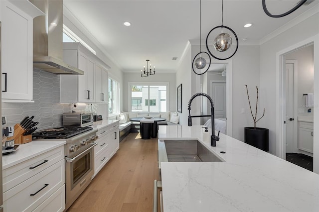 kitchen featuring crown molding, wall chimney exhaust hood, stainless steel stove, and a sink