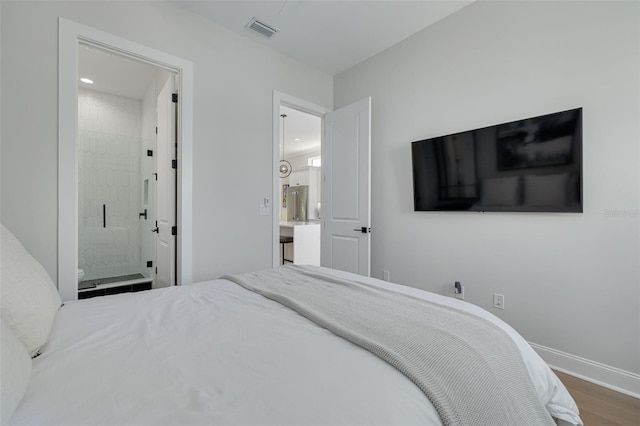 bedroom featuring ensuite bath, visible vents, wood finished floors, and baseboards