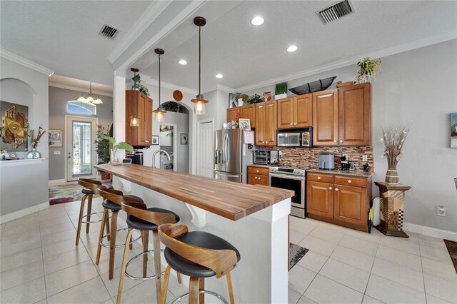 1102 Emerald Dunes Dr, Sun City Center, FL 33573 - kitchen featuring a breakfast bar, backsplash, crown molding, light tile patterned flooring, and appliances with stainless steel finishes