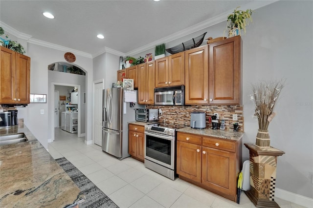 1102 Emerald Dunes Dr, Sun City Center, FL 33573 - kitchen with baseboards, crown molding, backsplash, brown cabinetry, and stainless steel appliances