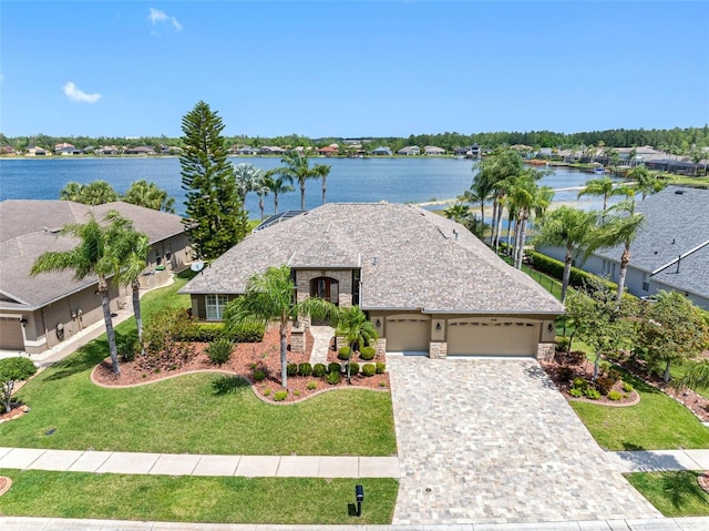 view of front facade with stone siding, decorative driveway, a water view, a front yard, and a garage