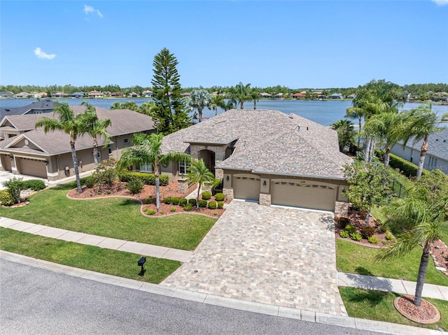 ranch-style house featuring driveway, stone siding, an attached garage, a front lawn, and a water view