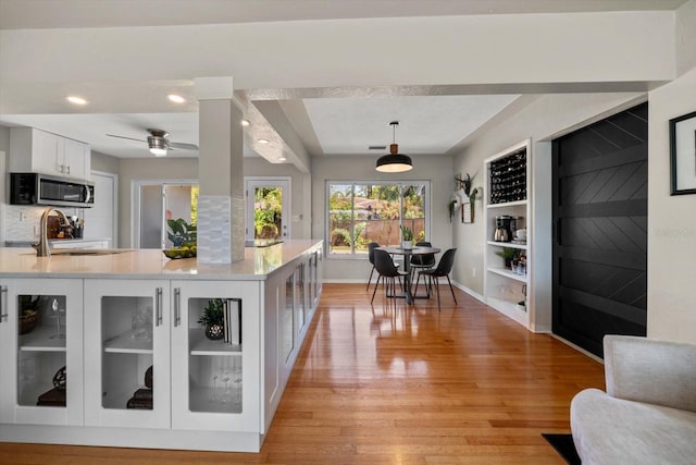 kitchen with light countertops, stainless steel microwave, baseboards, light wood finished floors, and white cabinets