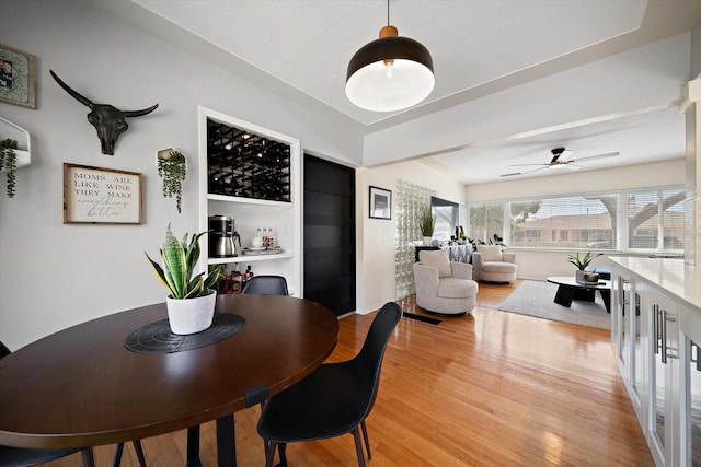 dining space with a bar, ceiling fan, and light wood finished floors