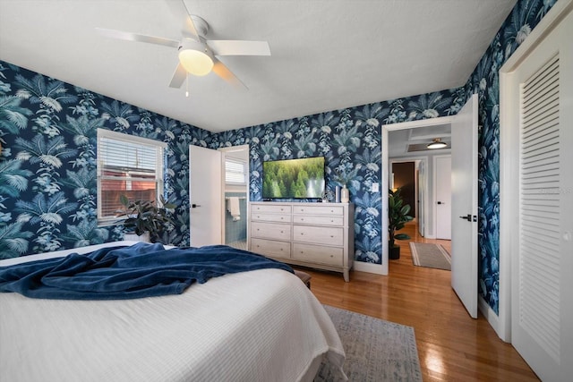 bedroom with a ceiling fan, wallpapered walls, a closet, and wood finished floors