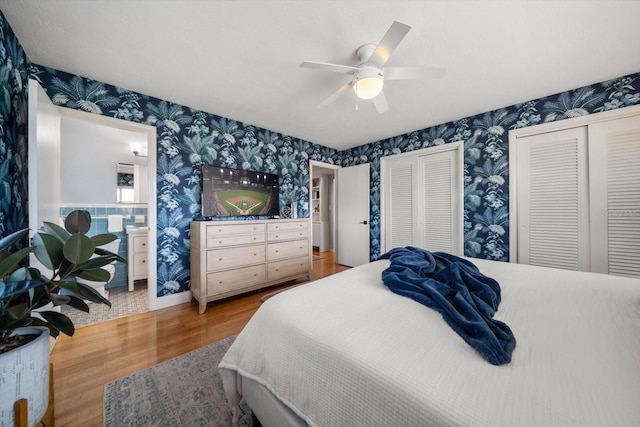 bedroom featuring multiple closets, ceiling fan, wallpapered walls, and wood finished floors