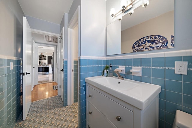 bathroom featuring toilet, vanity, wainscoting, tile patterned flooring, and tile walls