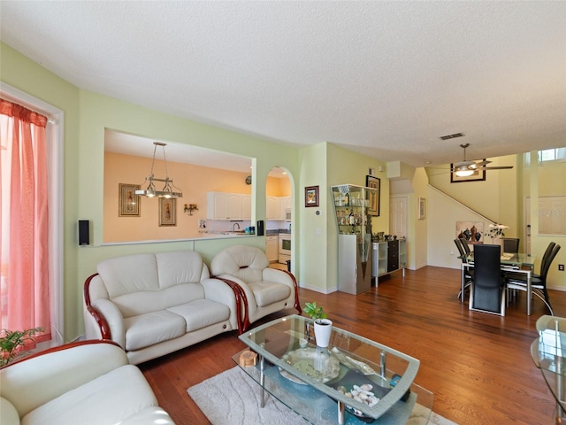 living room featuring arched walkways, wood finished floors, visible vents, and a textured ceiling