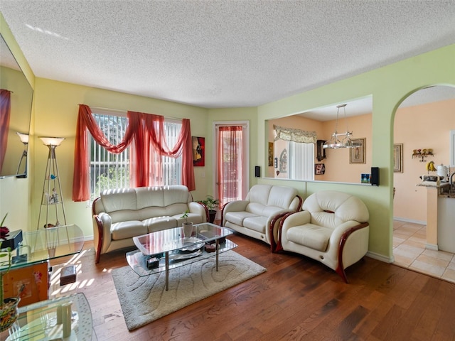 living room featuring a textured ceiling, wood finished floors, baseboards, and arched walkways