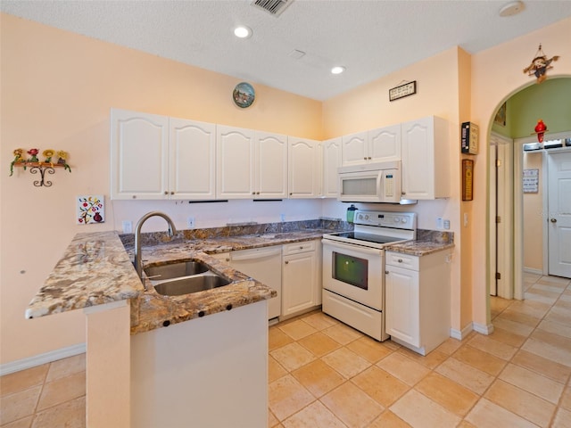 kitchen with stone countertops, a peninsula, a sink, and white appliances