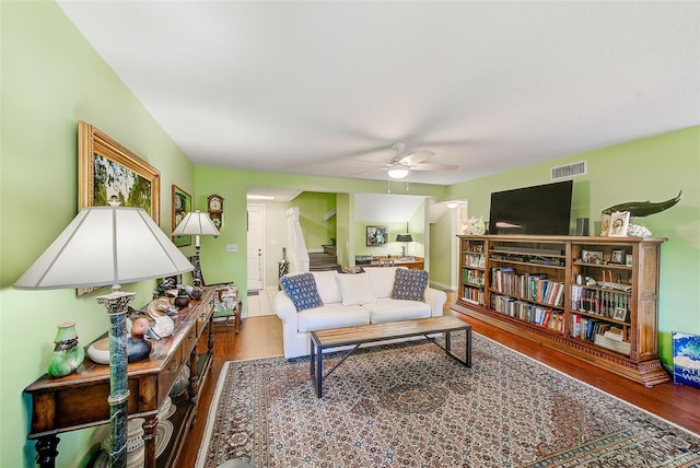 living room featuring stairway, visible vents, a ceiling fan, and wood finished floors