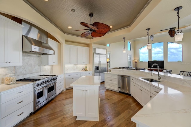 kitchen with a large island with sink, high quality appliances, a sink, wall chimney exhaust hood, and ceiling fan