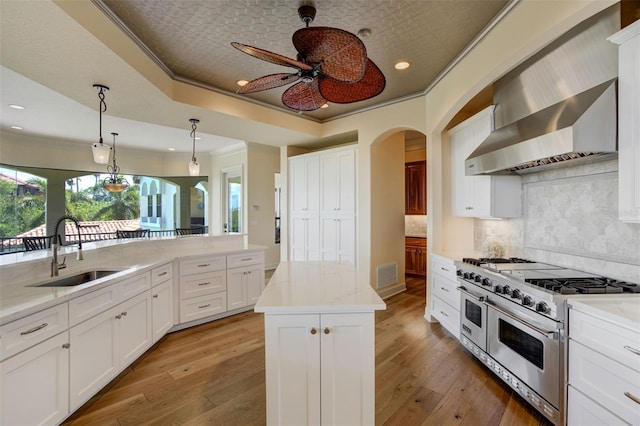 kitchen with crown molding, ceiling fan, a sink, double oven range, and wall chimney range hood