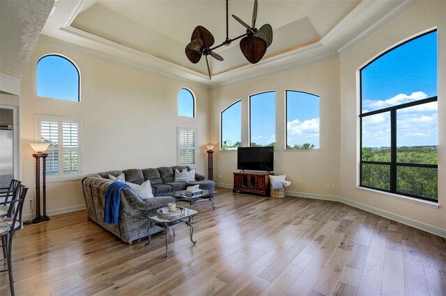 living area with a ceiling fan, a tray ceiling, baseboards, and wood finished floors