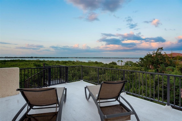 balcony at dusk featuring a water view