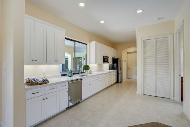 kitchen with light countertops, appliances with stainless steel finishes, arched walkways, white cabinetry, and a sink