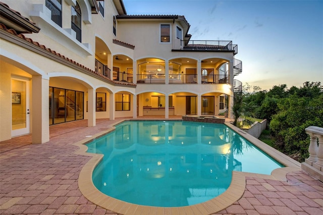 back of house at dusk featuring a balcony, a tiled roof, stucco siding, and a patio area