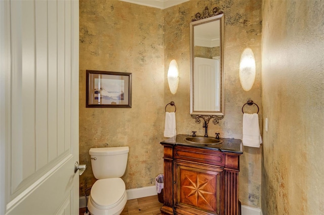 bathroom with baseboards, wallpapered walls, toilet, wood finished floors, and vanity