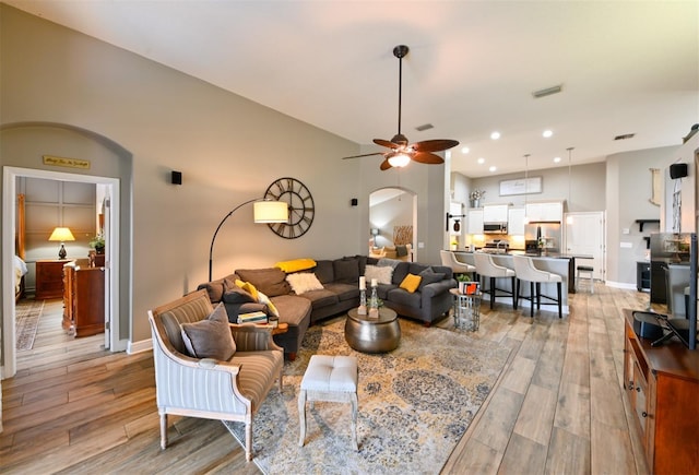living room with baseboards, a ceiling fan, light wood-style floors, visible vents, and arched walkways