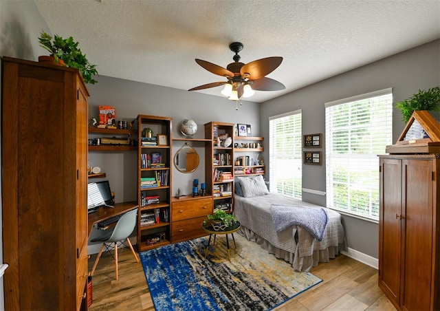 bedroom with baseboards, light wood-type flooring, a textured ceiling, and a ceiling fan