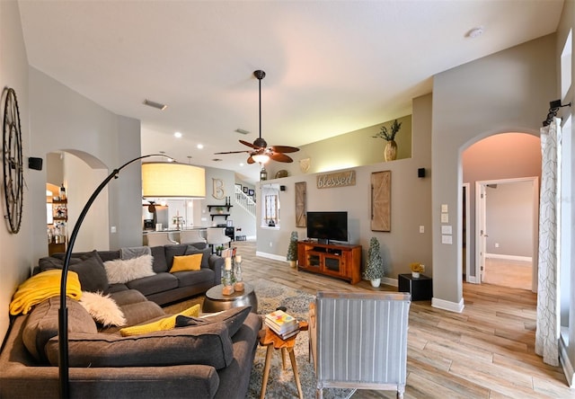 living area with visible vents, baseboards, arched walkways, a ceiling fan, and light wood-style flooring