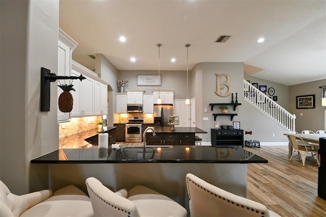 kitchen with light wood-style flooring, a peninsula, a kitchen bar, appliances with stainless steel finishes, and backsplash