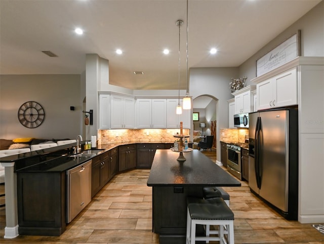 kitchen with arched walkways, a kitchen island, a breakfast bar, appliances with stainless steel finishes, and a sink