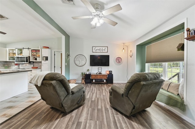 living area with visible vents, wood finished floors, lofted ceiling, and a ceiling fan