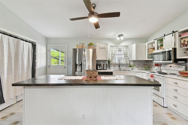 kitchen featuring stainless steel appliances, dark countertops, a kitchen island, a sink, and open shelves