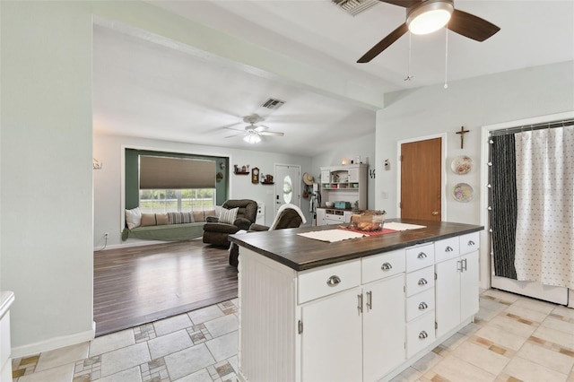 kitchen with white cabinetry, vaulted ceiling, dark countertops, visible vents, and ceiling fan