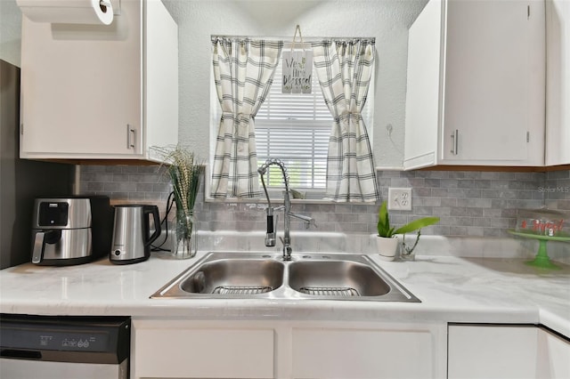 kitchen with decorative backsplash, light countertops, dishwasher, white cabinetry, and a sink