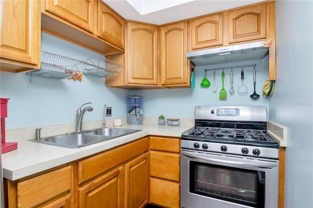 kitchen with stainless steel gas stove, light countertops, under cabinet range hood, a sink, and a skylight