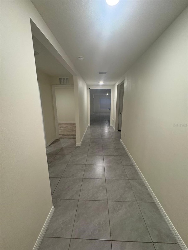hallway featuring light tile patterned floors, baseboards, and visible vents