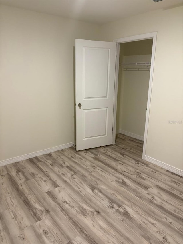unfurnished bedroom with baseboards, a closet, and light wood-type flooring