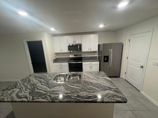 kitchen with a sink, dark stone countertops, light tile patterned floors, stainless steel appliances, and white cabinets
