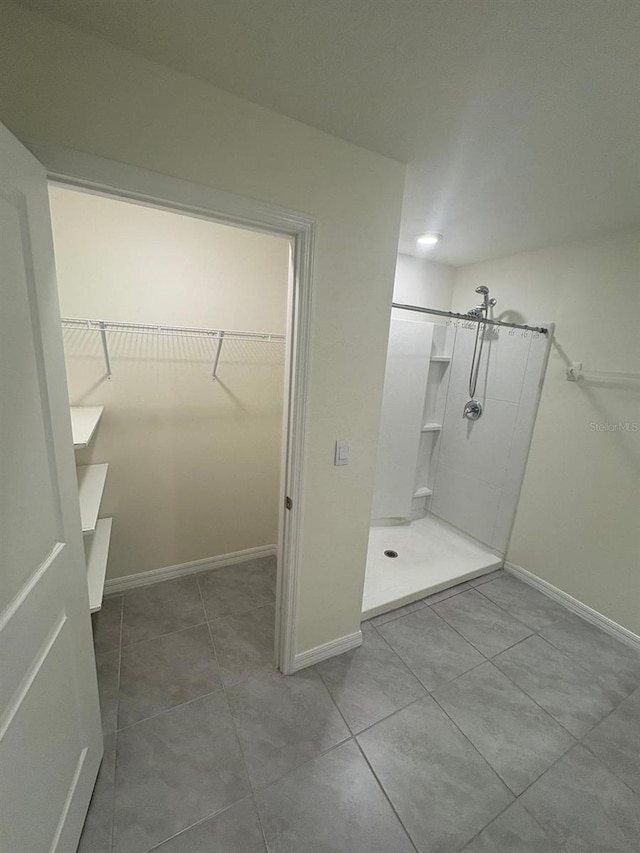 bathroom with a spacious closet, tile patterned floors, baseboards, and walk in shower