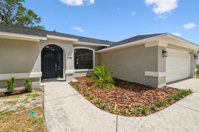 entrance to property with a garage, concrete driveway, stucco siding, and roof with shingles
