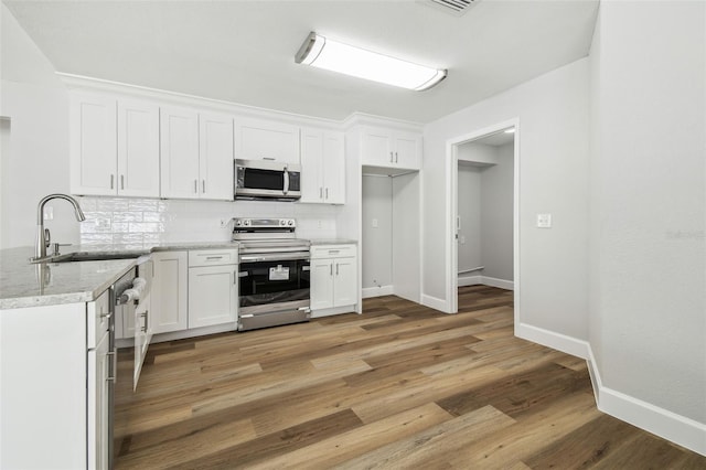 kitchen featuring white cabinetry, light wood-type flooring, stainless steel appliances, decorative backsplash, and a sink