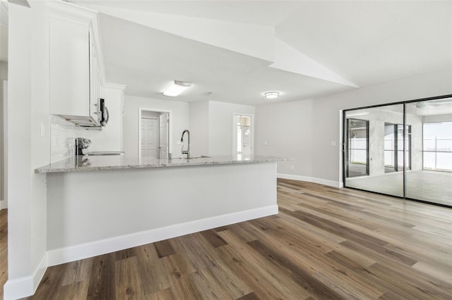 kitchen featuring white cabinets, a peninsula, wood finished floors, a sink, and light stone counters