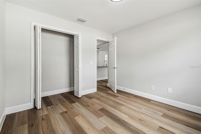 unfurnished bedroom featuring wood finished floors, a closet, baseboards, and visible vents
