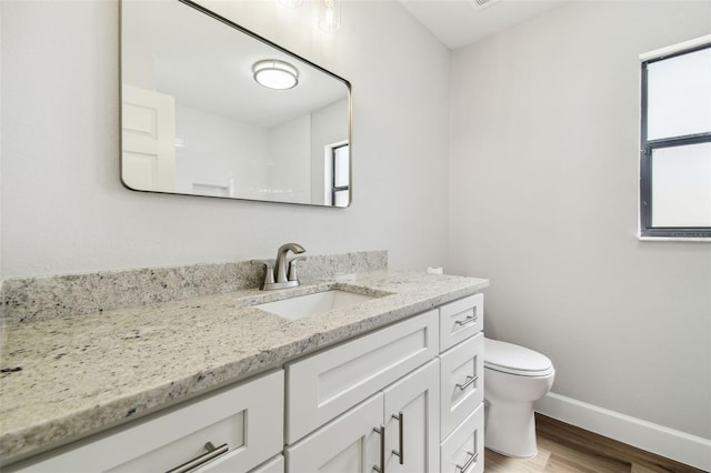 bathroom featuring baseboards, wood finished floors, toilet, and vanity