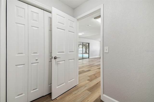 hallway featuring a textured wall, baseboards, and wood finished floors
