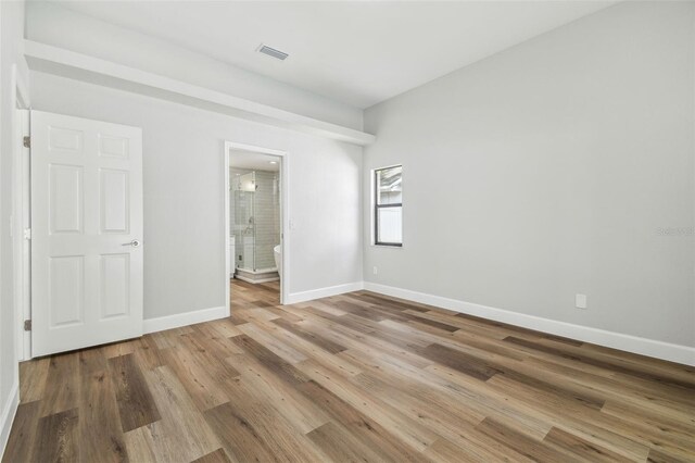 unfurnished bedroom featuring baseboards, visible vents, wood finished floors, and ensuite bathroom