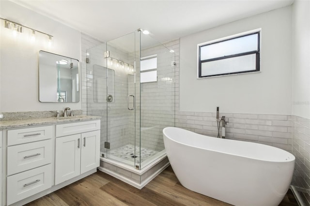 bathroom featuring tile walls, a soaking tub, wood finished floors, vanity, and a stall shower