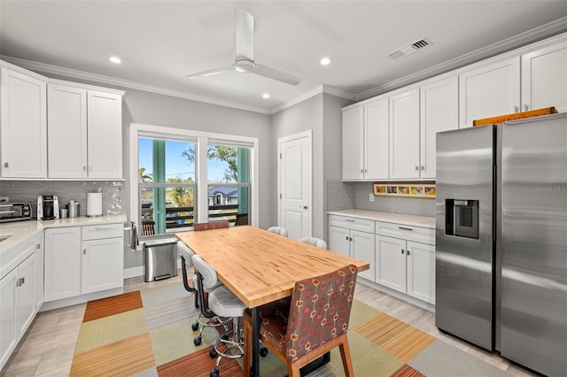 kitchen featuring crown molding, light countertops, stainless steel fridge, visible vents, and ceiling fan