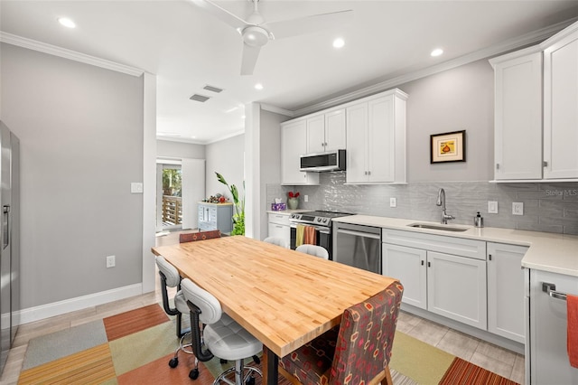 kitchen with light countertops, a sink, stainless steel appliances, decorative backsplash, and ornamental molding