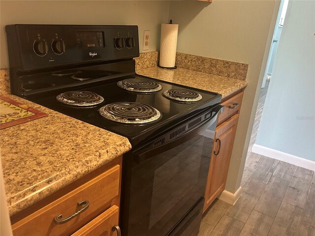 501 E Bay Dr Unit 2003, Largo, FL 33770 - kitchen with black range with electric stovetop, light wood-style floors, light countertops, baseboards, and brown cabinets
