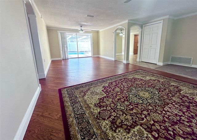 empty room featuring a textured ceiling, visible vents, ceiling fan, wood finished floors, and arched walkways