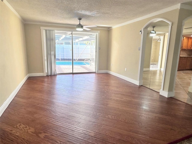 spare room with arched walkways, crown molding, ceiling fan, and wood finished floors