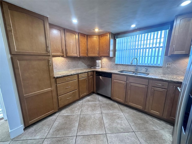 kitchen with stainless steel dishwasher, a sink, light stone counters, backsplash, and light tile patterned floors